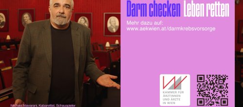 Der Kabarettist Michael Niavarani steht in einem mit roten Wänden und Bildern versehenen Raum.