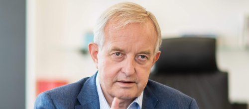 Mann mit Hemd und Sakko sitzt am Schreibtisch.