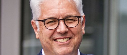 Mann mit Brille, Hemd und Sakko lächelt in die Kamera.