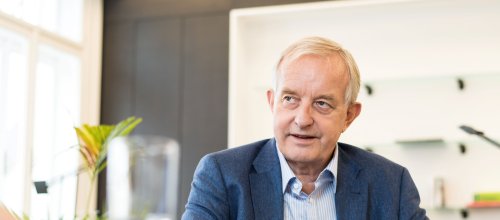 Präsident Johannes Steinhart sitzt an einem Tisch während eines Interviews und sieht dabei die Interviewerin an, von der man aber nur die Hand sehen kann.