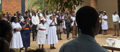Eine Aufnahme in einem Hof in Uganda. Es stehen mehrere Personen im Hof eines Spitals zur Morgenbesprechung. 