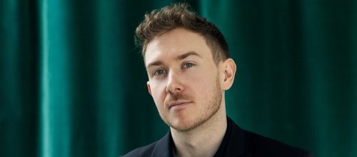 Eine Porträtaufnahme von Zukunftsforscher Tristan Horx - der ein dunkles Gewand trägt und im Hintergrund einen smaragdgrünen Vorhang hat.