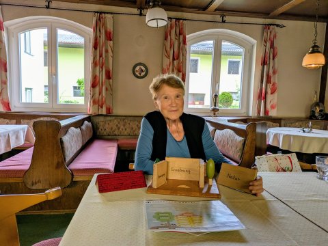 Maria Hengstberger sitzt auf einem Sessel an einem Tisch. Vor ihr, am Tisch, steht ihr Schutzhaus-Modell