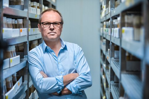 Gero Miesenböck, Neurophysiologe, lehnt sich an einem offenen Kasten-Ablage-System an, mit verschränkten Händen