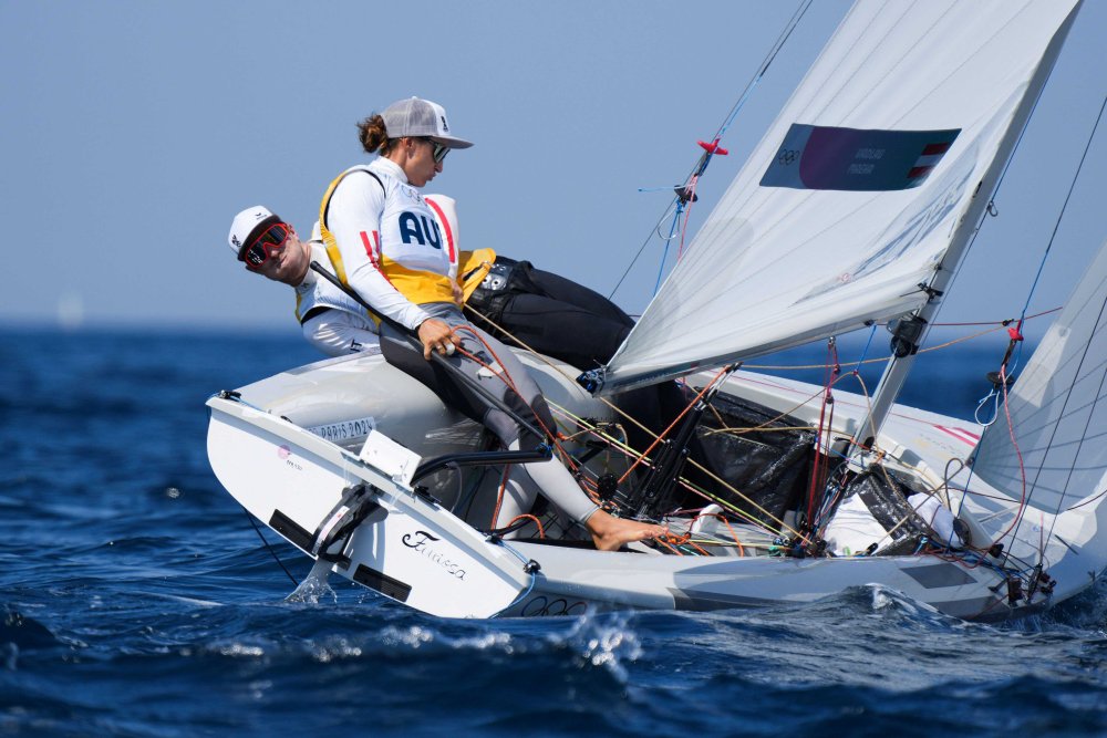 Zwei Personen, eine Frau und ein Mann, an Bord eines Segelboots, das sich im Wind stark neigt.